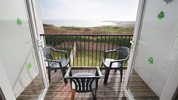 Ein Balkon mit zwei Stühlen und einem Tisch, der auf eine grüne Landschaft und Wasser blickt.