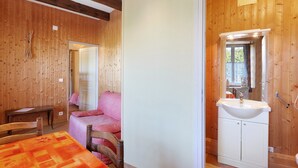 Un intérieur en bois comprenant un lit, une table et une salle de bain avec un lavabo et un miroir.