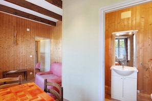 A wooden interior with a bed, a table, and a bathroom with a sink and mirror.