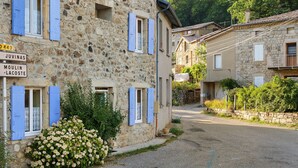 Un bâtiment en pierre avec des volets bleus, un chemin de gravier et une pancarte indiquant « Juvinas » et « Moulin-Lacoste ».