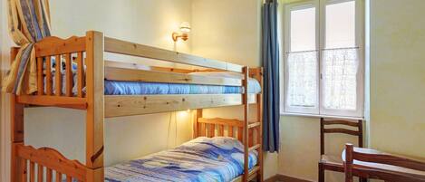 A bunk bed room with a window, a chair, and a wall-mounted light fixture.