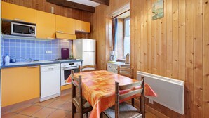 Une cuisine compacte équipée d’un four à micro-ondes, d’une cuisinière et d’un évier, avec des murs en bois et un coin repas comprenant une table et des chaises.