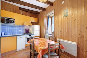 A compact kitchen with a microwave, stove, and sink, wooden walls, and a dining area with a table and chairs.