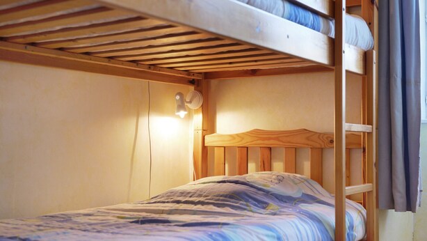 Un lit superposé avec un lit simple en haut et un lit simple en bas. Un luminaire est fixé au mur au-dessus du lit supérieur.