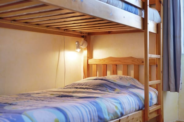 A bunk bed with a single bed on top and a single bed below. There is a wall-mounted light fixture above the top bunk.