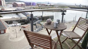 Un balcon avec une table, des chaises et une vue sur une rivière et des bâtiments.