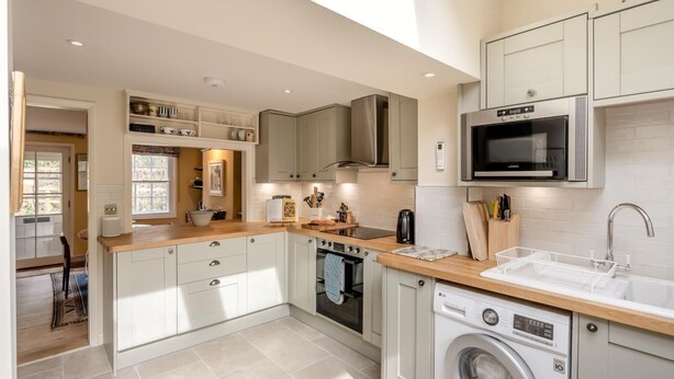 A compact kitchen with a microwave, oven, and washing machine, featuring white cabinetry and a wooden countertop. - 2 Bed in Chelmondiston (oc-s34724) (Pin Mill)
