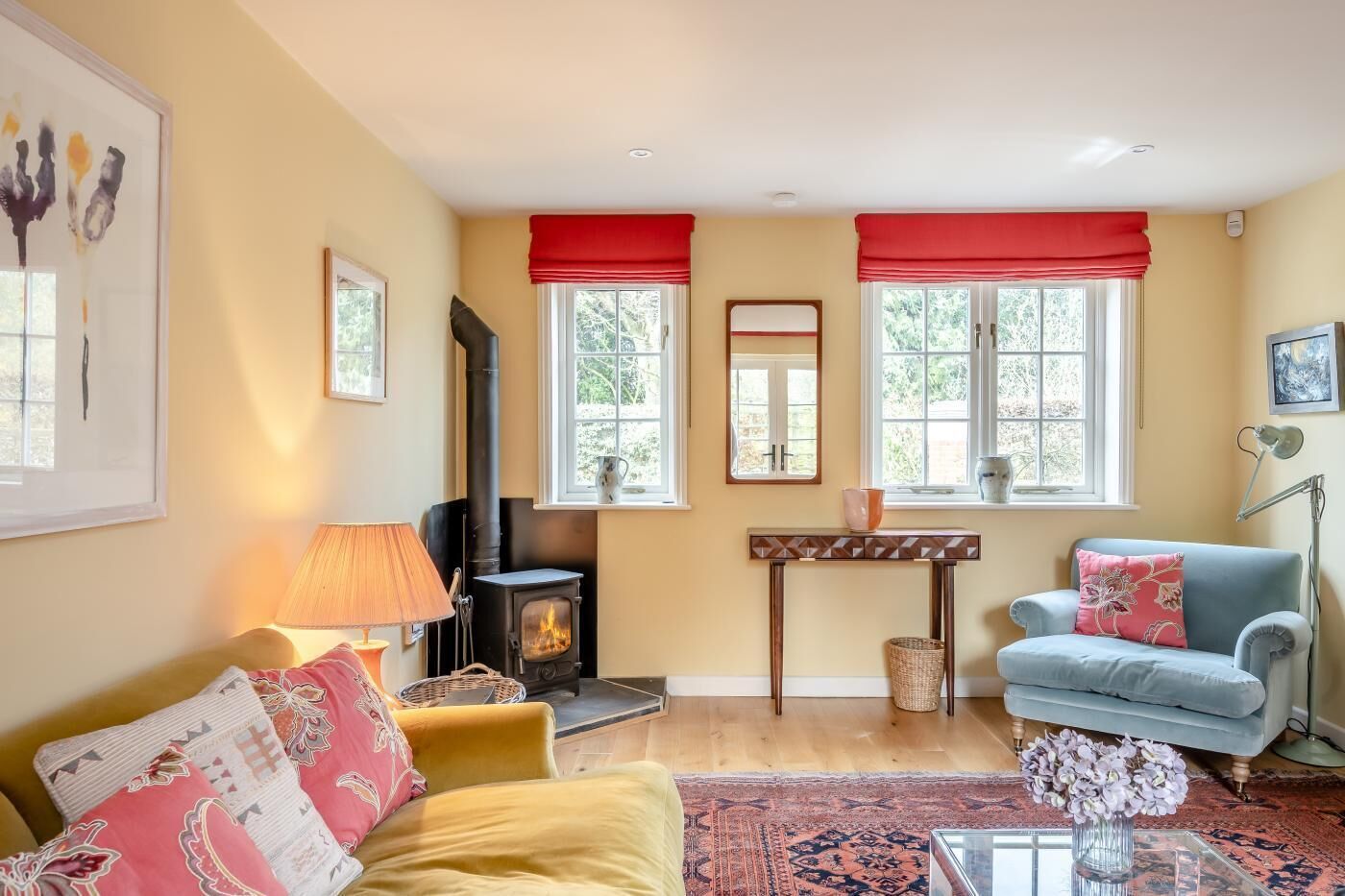 Una sala de estar acogedora con chimenea, un sofá, un sillón azul y una mesa con un jarrón de flores.