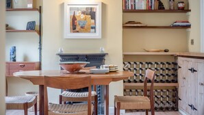 A dining area with a round wooden table, two wicker chairs, a bowl, and plates. - 2 Bed in Chelmondiston (oc-s34724) (Pin Mill)