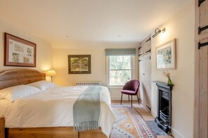 Ein Schlafzimmer mit Bett, Sessel, Kamin und gerahmten Bildern an den Wänden.