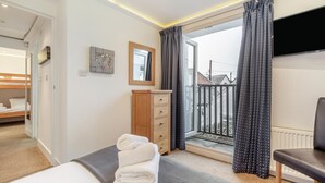 A hotel room with a bed, a wooden dresser, a TV, and a balcony with curtains. - 4 Bed in Braunton (oc-n34220) (Braunton)