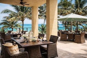 An outdoor dining area with wicker furniture, a table set with wine glasses, and a view of the ocean. - Remodel full amenity condo at the palm beach Marriott singer island beach resort (Riviera Beach)
