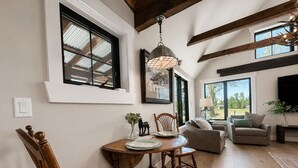 A dining area with a wooden table and chairs, a chandelier, and a large window with a view.