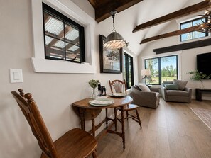 A dining area with a wooden table and chairs, a chandelier, and a large window with a view.
