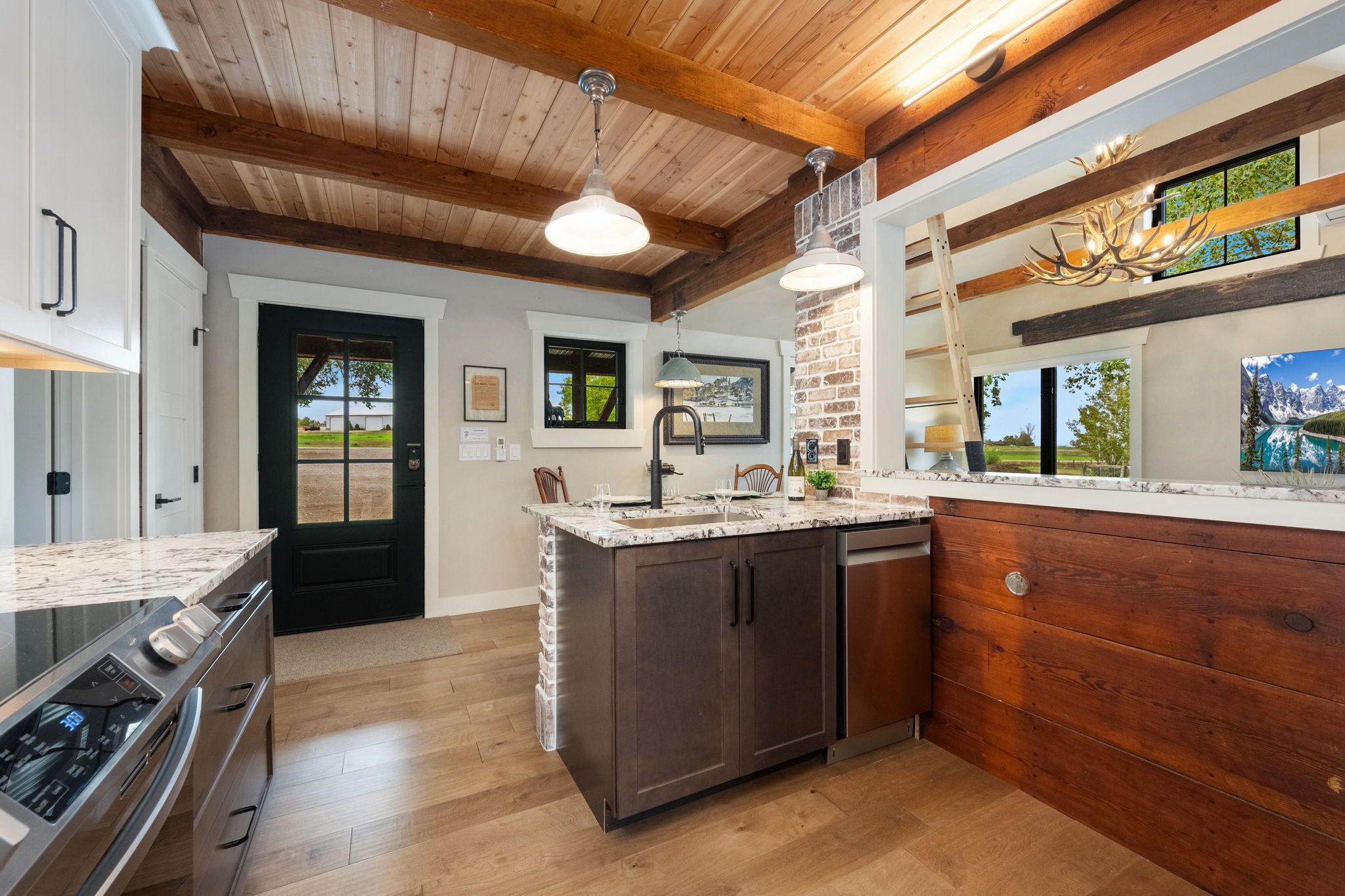 A modern kitchen with a central island, wooden beams on the ceiling, and a view of the outdoors through a window.