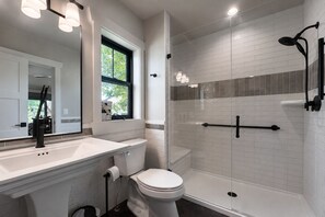 Un baño moderno con tocador blanco, inodoro, ducha con mampara de vidrio y un espejo grande.