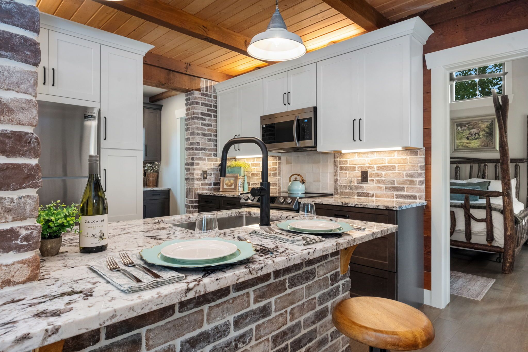 A kitchen with a stone backsplash, white cabinets, a stainless steel refrigerator, and a wooden ceiling.
