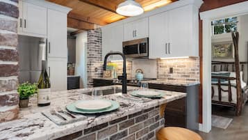 A kitchen with a stone backsplash, white cabinets, a stainless steel refrigerator, and a wooden ceiling.