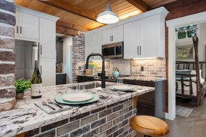 Una cocina con salpicadero de piedra, armarios blancos, refrigerador de acero inoxidable y techo de madera.