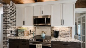 A kitchen with white cabinets, a stainless steel microwave, a gas stove, and a brick wall.