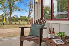 Una silla de madera con un cojín, una mesa con dos botellas de cerveza, un libro y una planta en maceta.