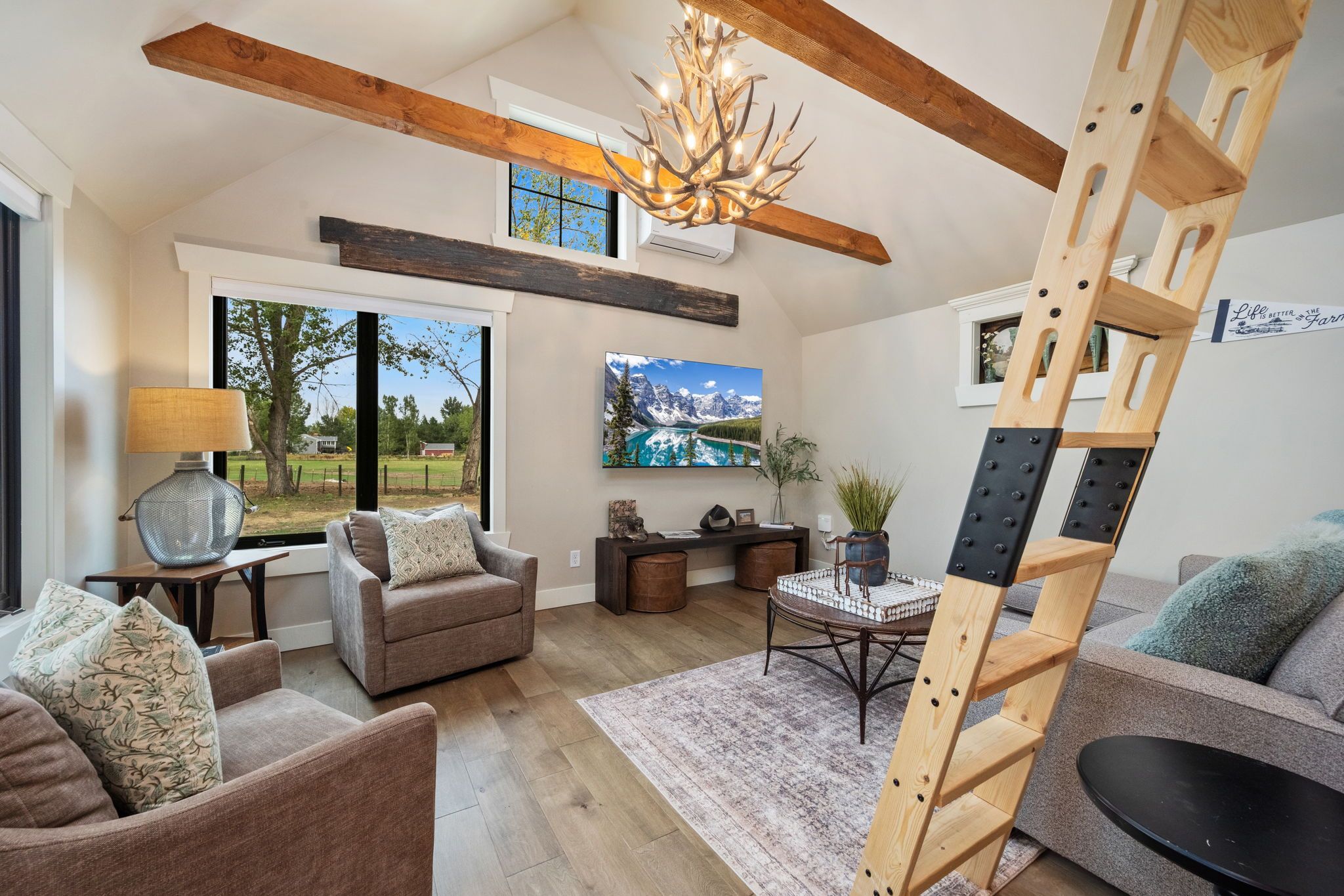 A spacious living room with a large window, a fireplace, a chandelier, and a ladder.