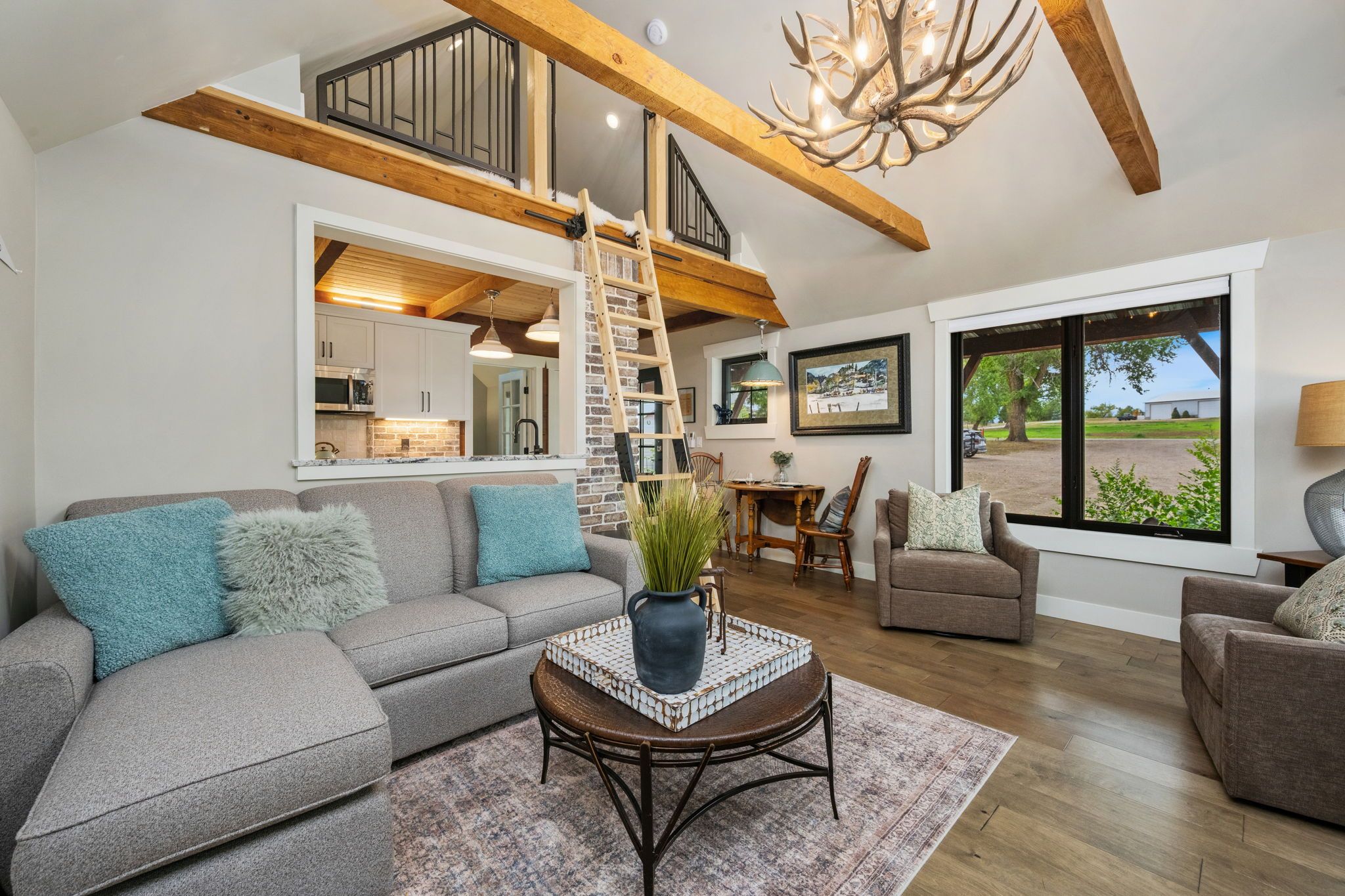 A spacious living area with a high ceiling, a staircase, a dining area, and a view through large windows.