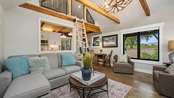 A spacious living area with a high ceiling, a staircase, a dining area, and a view through large windows.