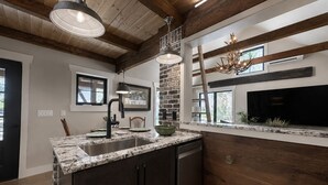 A kitchen with a stone backsplash, wooden beams, a built-in stove, and a large window.