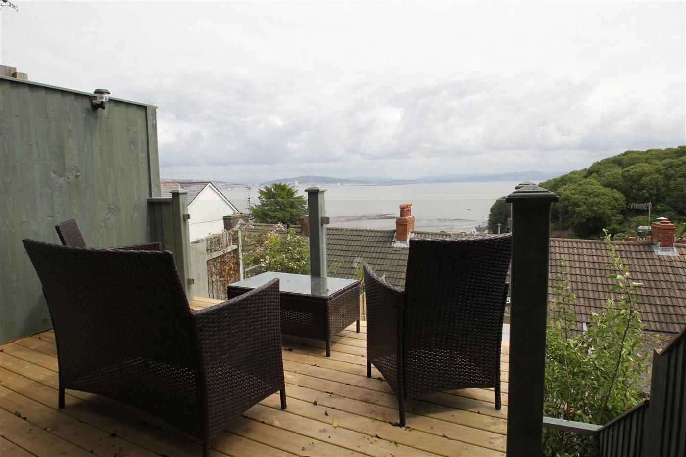 A wooden deck with wicker furniture, overlooking a body of water and greenery.