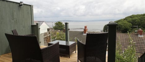 A wooden deck with wicker furniture, overlooking a body of water and greenery.