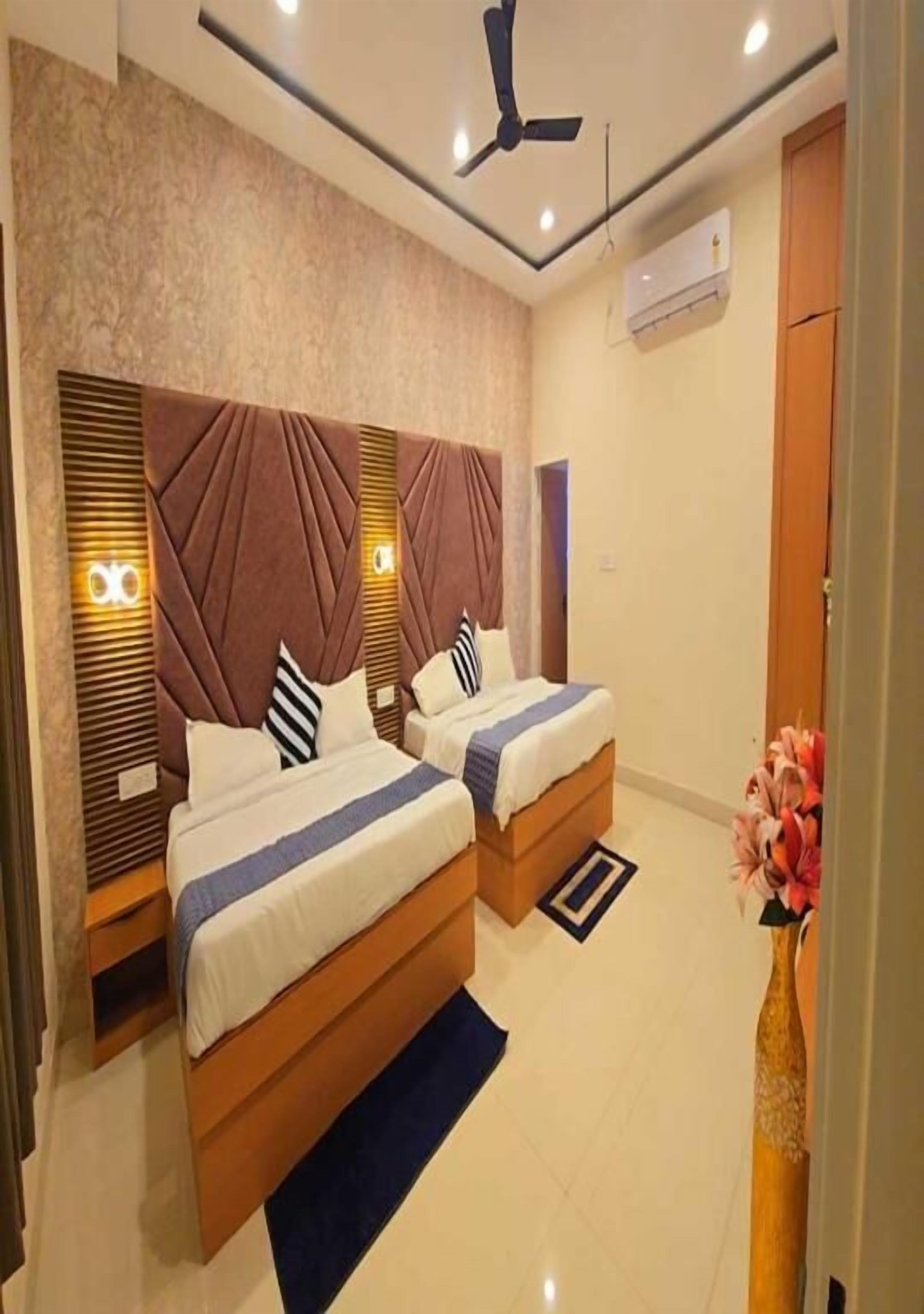 Habitación de hotel con dos camas, un ventilador de techo, un florero con flores y una alfombra pequeña.