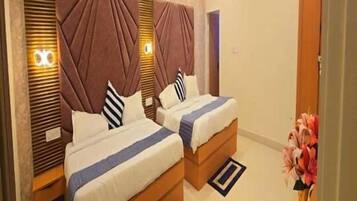Habitación de hotel con dos camas, un ventilador de techo, un florero con flores y una alfombra pequeña.