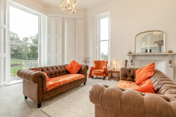 A spacious living room with a large window, a fireplace, and two brown leather sofas with orange cushions. - 3 Bed in Torquay (oc-r34662) (Torquay)