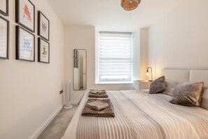 A bedroom with a bed, pillows, a bedside table, a lamp, a window with blinds, and framed pictures on the wall. - 3 Bed in Torquay (oc-r34662) (Torquay)