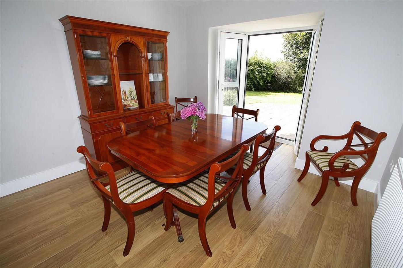 Une salle à manger avec une table et des chaises en bois, un buffet, et une vue à travers une porte vitrée.
