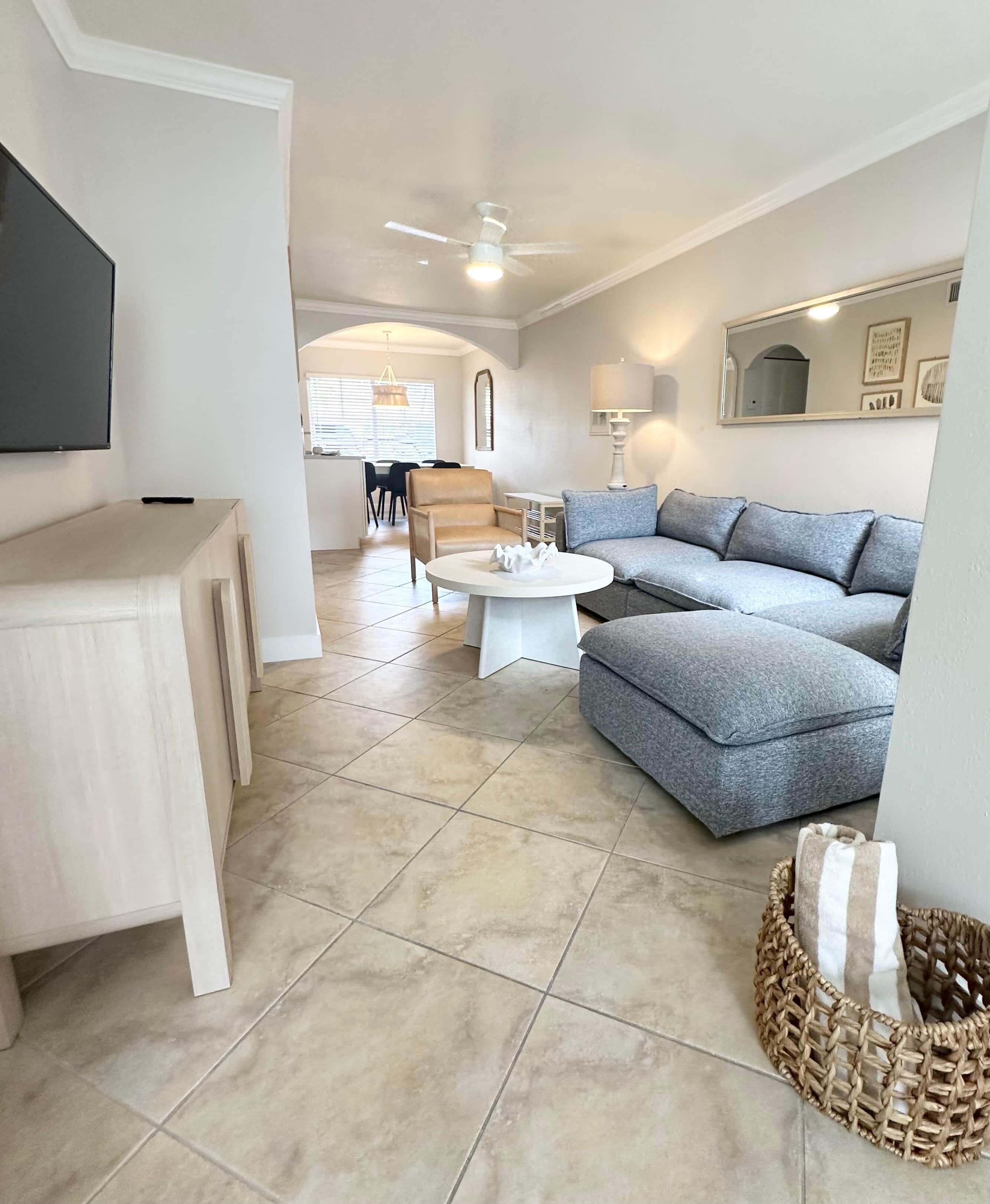 A modern living room with a sectional sofa, a coffee table, and a flat-screen TV mounted on the wall.