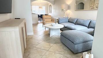 A modern living room with a sectional sofa, a coffee table, and a flat-screen TV mounted on the wall.