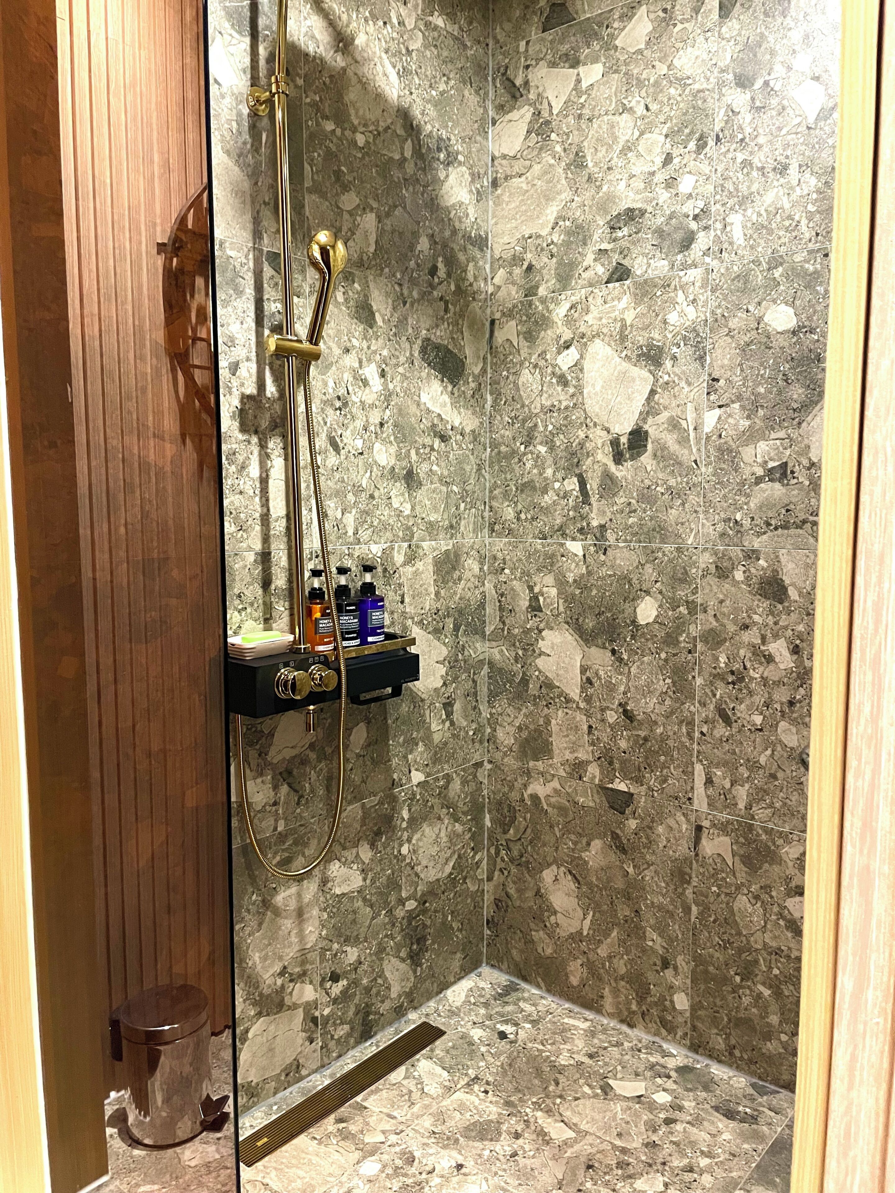 Una ducha con pared de mármol, puerta de madera y repisa con artículos de aseo.