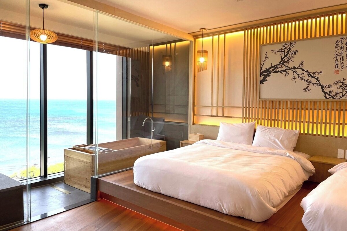 A modern bedroom with a large bed, a bathtub, and a view of the ocean.