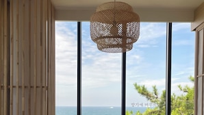 Une pièce dotée d’une grande fenêtre, d’un luminaire au plafond fait de fibres tressées et offrant une vue sur la mer.