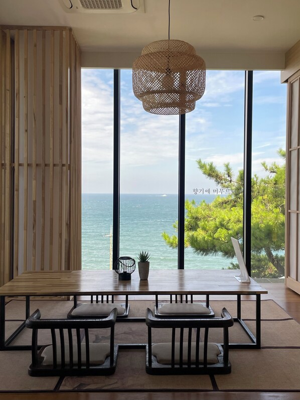 Une pièce dotée d’une grande fenêtre, d’un luminaire au plafond fait de fibres tressées et offrant une vue sur la mer.