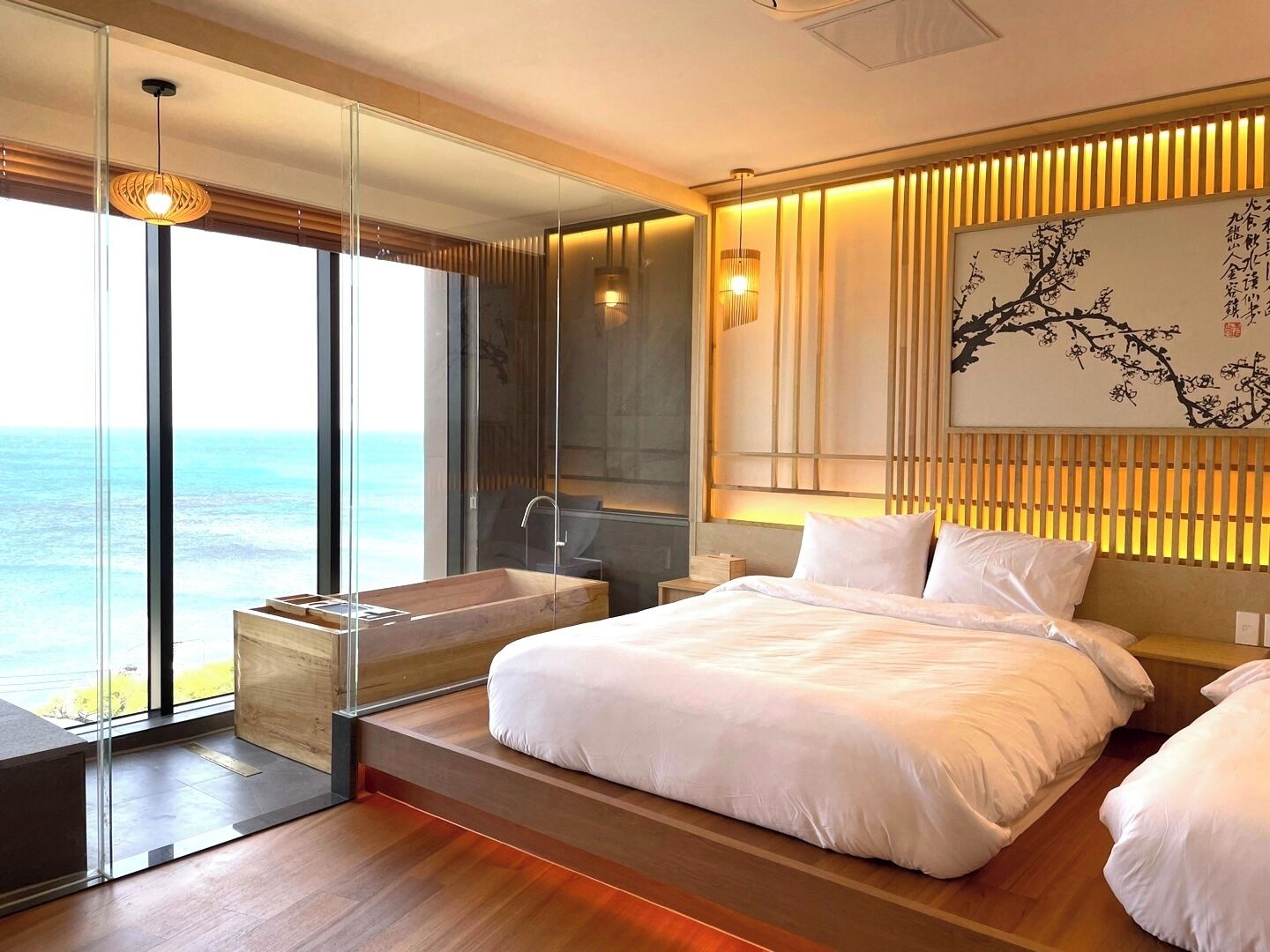 A modern bedroom with a large bed, a bathtub, and a view of the ocean.