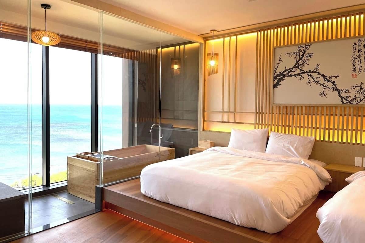 A modern bedroom with a large bed, a bathtub, and a view of the ocean.