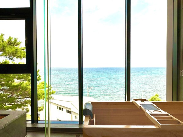 A room with large windows overlooking a body of water, a wooden bench, and a small table. - One Fine Day Aewol (Jeju)