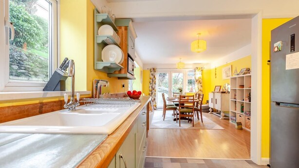 A kitchen with a sink, a dining area with chairs, and a refrigerator. - 3 Bed in Ilfracombe (oc-s34501) (Ilfracombe)