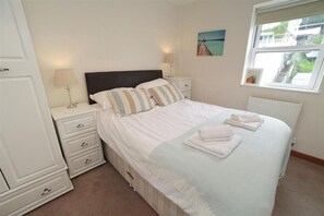 A neatly arranged bedroom with a bed, bedside tables, a lamp, a radiator, and a window with a view.