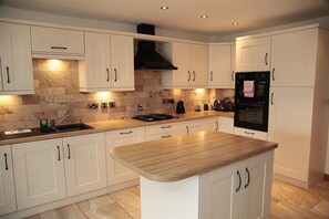 A modern kitchen with white cabinetry, a central island, a stove, and a built-in oven. - 4 Bed in Mumbles (oc-hh114) (The Mumbles)