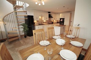 Une cuisine moderne avec des meubles blancs, un réfrigérateur noir et un coin repas doté d’une table en bois, mise pour quatre personnes.