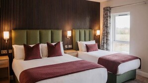 A hotel room with two beds, each with a green headboard, white bedding, and a red throw blanket. There are bedside lamps and a window with a view. - Kerry Coast Hotel (Cahirciveen)